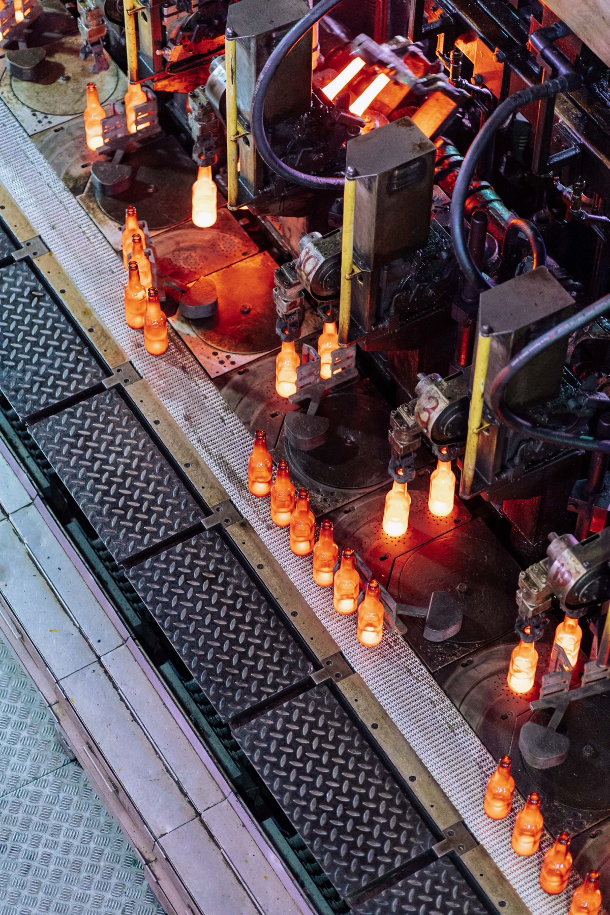 Glowing glass bottles moving through an automated forming line.