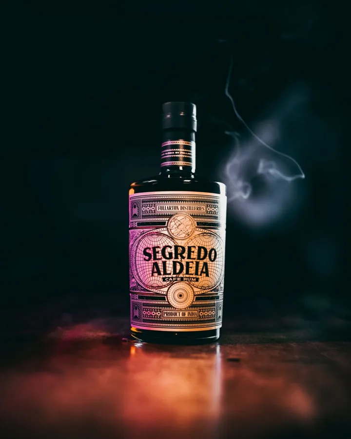 Single Segredo Aldeia Cafe Rum bottle with straight sidewalls, short neck and dark closure, dramatic teal background and warm reflection.