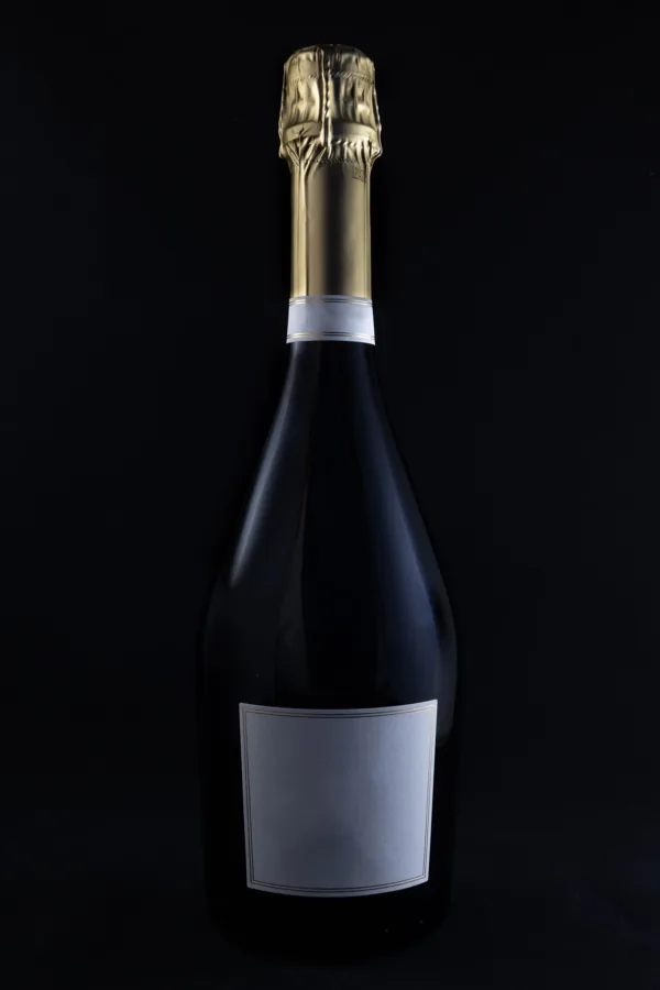 Full broad-shouldered sparkling bottle, gold foil, blank pale label against black. Strong portrait product image.