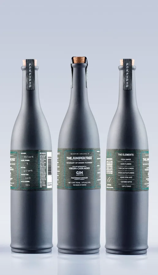 Three tall matte charcoal gin bottles on neutral grey, long tapered shoulders with natural corks.