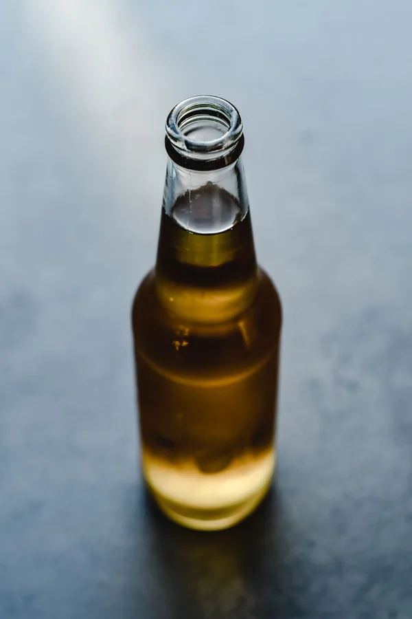 Full uncapped amber beer bottle from a slightly elevated angle on blue-gray surface. Natural light and shallow focus.